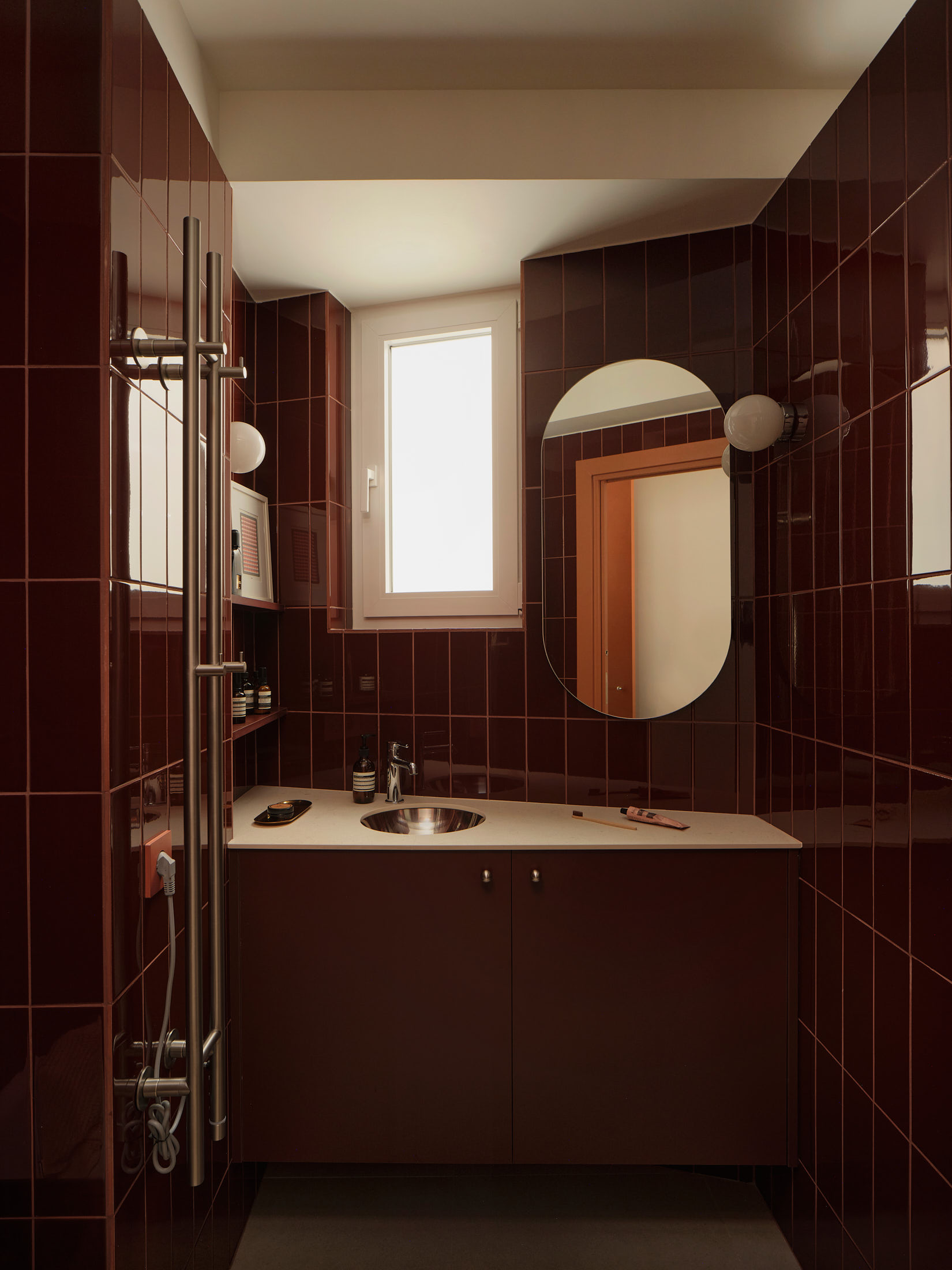 Viladomat Apartment in Barcelona by Colombo Architecture - bathroom clad in cherry red tiles with oval mirror